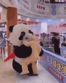 a panda mascot is holding a stuffed animal in his arms in a mall .