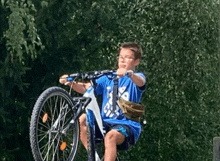 a young boy is sitting on a bicycle with a bag on his shoulder .