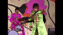 a man in a green suit is playing a guitar while another man in a pink suit plays drums