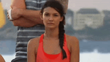 a woman in a red tank top is looking at the camera while standing next to a man .
