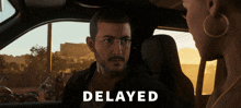a man sitting in a car talking to a woman with the word delayed above him