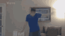 a man in a blue shirt is dancing in a living room with the word wave on the wall behind him