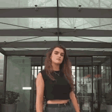 a woman wearing a black crop top and blue jeans is standing in front of a building .