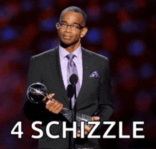a man in a suit and tie holds a trophy in front of a microphone with the words 4 schizzle behind him