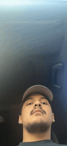 a man with a beard wearing a hat and earrings looks at the camera