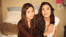 two women are sitting next to each other on a bed and hugging each other .
