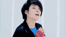 a young man wearing a blue shirt and a black jacket is wearing a pair of red gloves