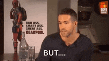 a man is sitting at a table with a bottle of water and a poster of deadpool on the wall .