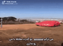 a red car is sitting in the middle of a dirt field with a blue sky in the background .