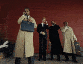 a group of men standing in front of a red wall talking on their cell phones