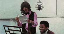a man in a pink shirt is singing into a microphone next to another man