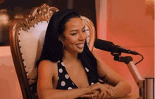 a woman in a black and white polka dot dress sits in a chair in front of a microphone