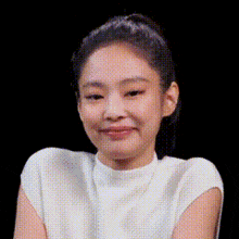 a close up of a woman 's face with a black background . she is wearing a white shirt and smiling .