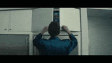 a man in a blue shirt is reaching into a cabinet for a box of oreos