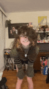 a girl with curly hair is standing in a room with a picture of a man and woman on the wall .