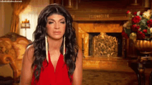 a woman in a red dress is standing in front of a fireplace .