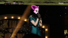 a woman wearing a cat mask is singing into a microphone on a mbc channel