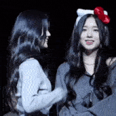 two girls are standing next to each other in a dark room . one girl is wearing a hello kitty headband .