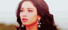 a close up of a woman 's face wearing earrings and looking at the camera .