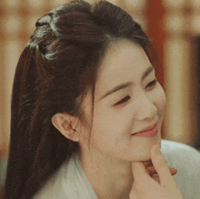 a woman with long hair is smiling with her hand on her chin