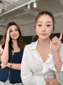 two women standing next to each other one wearing a white shirt and the other wearing a blue tank top