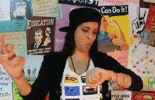 a woman wearing a hat stands in front of a wall with a poster that says education