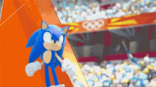 sonic the hedgehog is standing in front of a stadium with the olympic rings