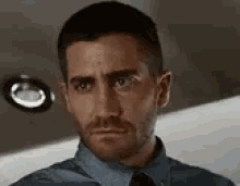 a man with a beard and a blue shirt and tie is looking at the camera .