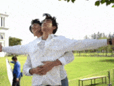 two men in white shirts are hugging each other in a park .