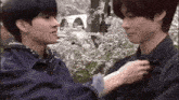 two young men are standing next to each other in front of a tree .
