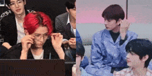 a group of young men are sitting in front of a laptop computer . one of the men is wearing glasses .