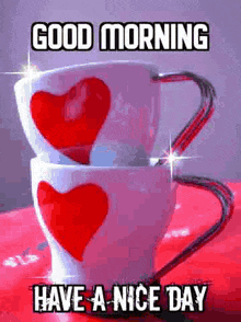 two coffee cups with red hearts on them are stacked on top of each other on a red table .