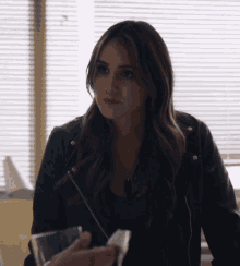 a woman in a black leather jacket holds a glass in her hand