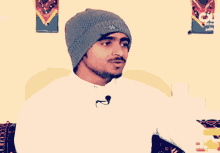 a man wearing a white shirt and a gray beanie has a microphone on his neck