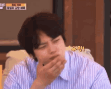 a man in a blue striped shirt is covering his mouth with his hand .