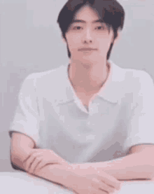 a young man in a white shirt is sitting at a table with his hands folded .
