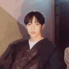 a young man wearing a black jacket and a white shirt is sitting down .
