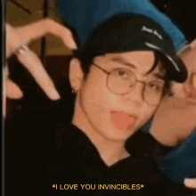 a man wearing glasses and a hat making a heart shape with his hands .