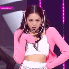 a woman in a pink jacket and white top is singing into a microphone on stage .