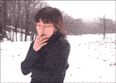a woman is smoking a cigarette in the snow while standing in the snow .