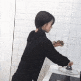 a woman in a black sweatshirt is cooking on a stove