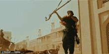 a man holding a spear in front of a building with the words pranay varma below him