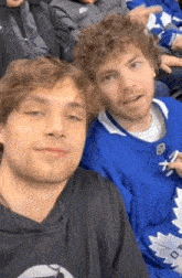 two men are sitting next to each other in a stadium and one of them is wearing a maple leaf jersey .