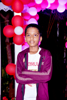 a young boy wearing a formula shirt stands with his arms crossed in front of pink balloons