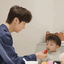 a man feeds a baby a strawberry with a spoon