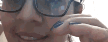 a woman wearing glasses and blue nail polish is scratching her face .