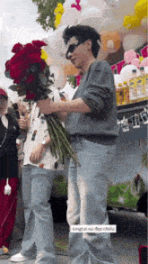 a man is holding a large bouquet of red roses while standing in front of balloons .