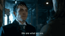 a man in a suit and tie is talking to another man and saying we are what we are .
