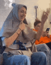 a woman wearing a hijab is sitting on a couch with a man looking at his phone .