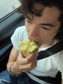 a man with curly hair is eating an apple in a car